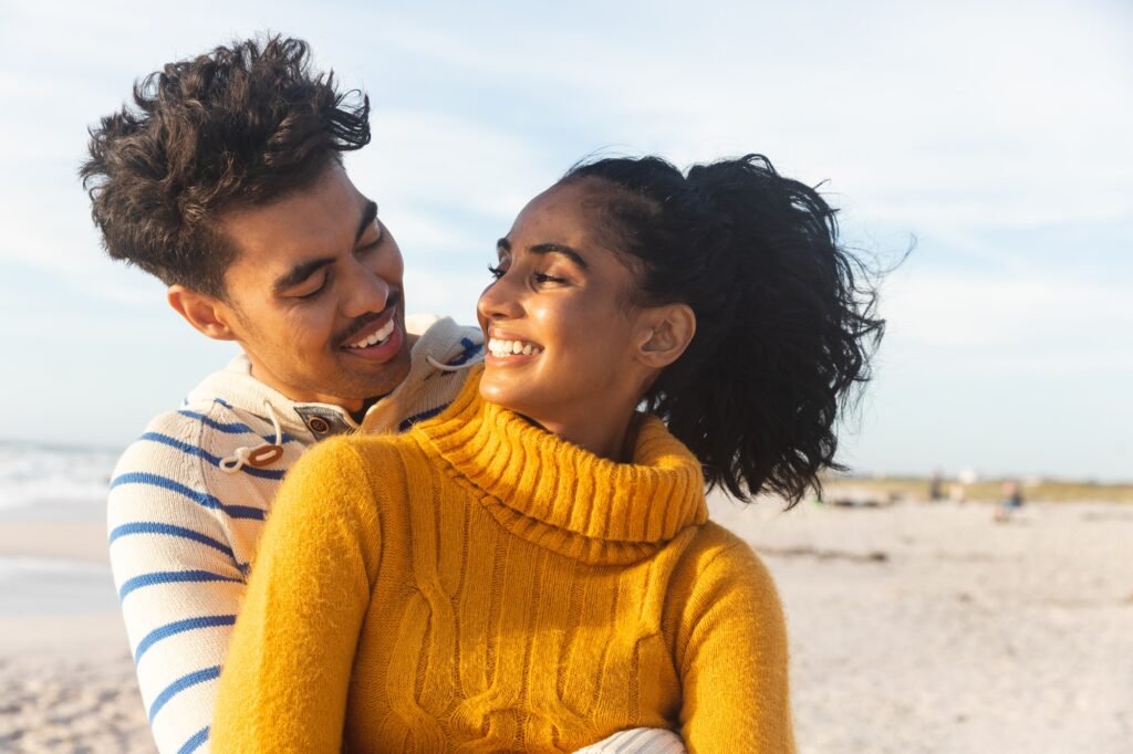 Smiling multiracial couple looking at each other while enjoying sunny day on beach